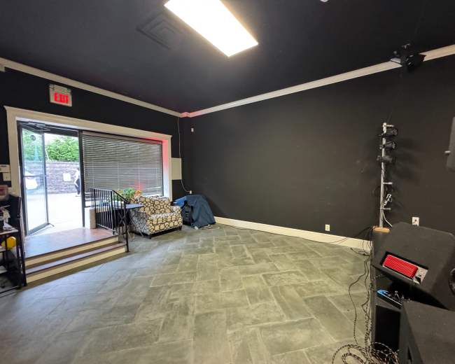 The image shows an empty room with black walls, a tiled floor, a couch in the corner, and a small staircase leading to an exit.