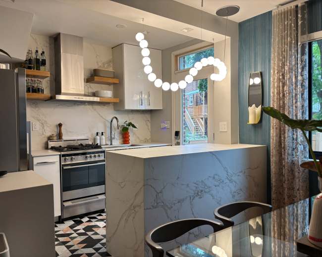 The image shows a modern kitchen featuring a sleek countertop, a gas stove, and decorative lighting, complemented by a window view and geometric floor tiles.
