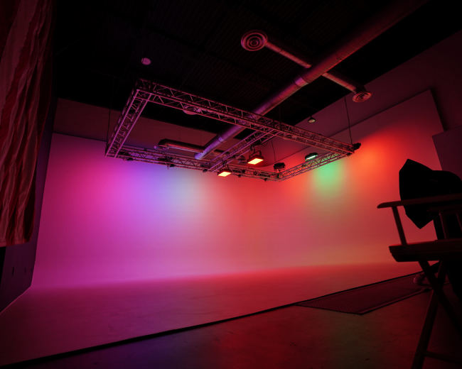 A photography studio with a colorful gradient backdrop and a lighting rig suspended from the ceiling.
