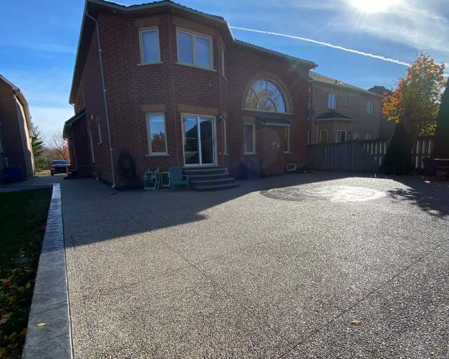 A brick house features a large driveway with a circular design, under a clear blue sky with the sun shining brightly.