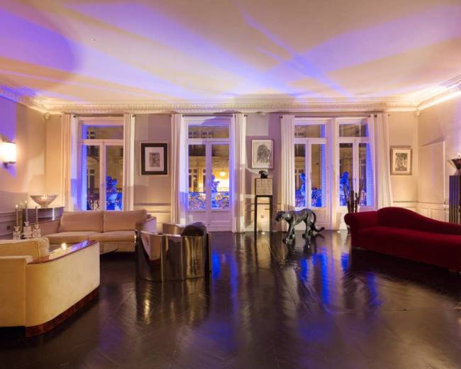 The image shows a spacious room with elegant furnishings, large windows allowing natural light, and a mix of modern and classic decor.