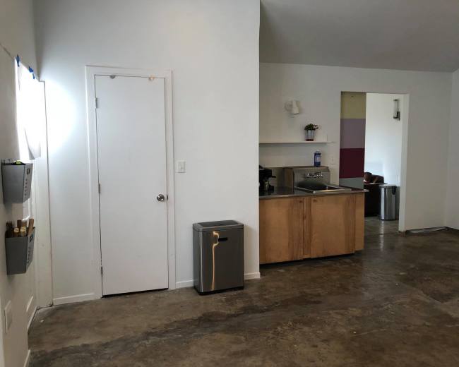 A kitchen area with a countertop and sink is visible, along with a door leading to another room and a trash bin on the floor.