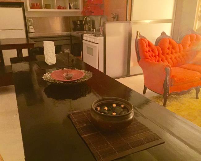 A modern kitchen and living area featuring an orange tufted sofa, a black dining table, and decorative items on the table.