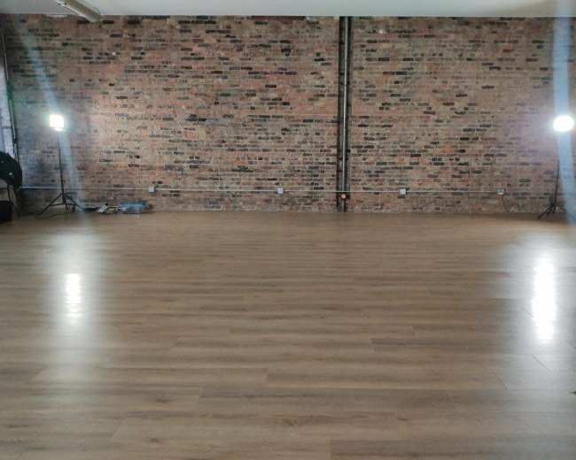 A spacious room features a wooden floor and exposed brick walls, illuminated by two standing lights.