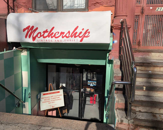 The image shows the entrance to "Mothership Vintage and Thrift," located below a staircase with an open sign visible in the window.
