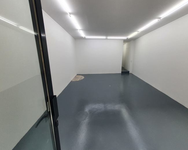 An empty room with a smooth gray floor and white walls, illuminated by overhead lighting.