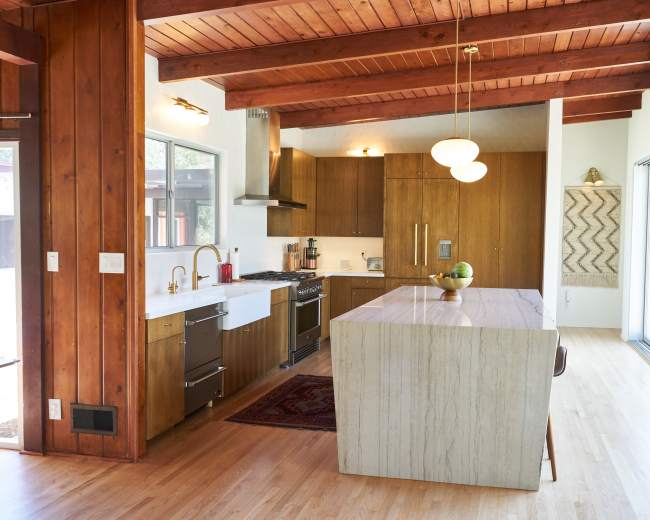 The image shows a modern kitchen with wooden beams, a marble-topped island, and contemporary appliances.