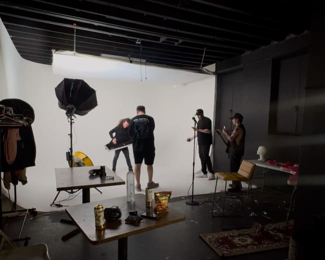 A group of four people is working in a photography studio, with one person posing in front of a bright white backdrop while others assist and set up equipment.