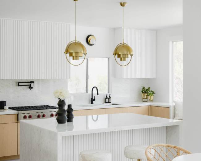 The kitchen features a marble island with gold accents, light wooden cabinetry, and modern pendant lighting.
