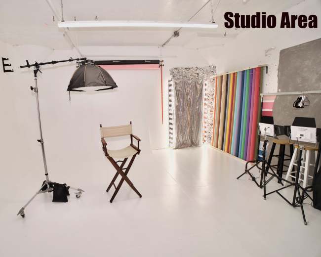 The image shows a bright, empty photography studio with a director's chair, lighting equipment, and a colorful backdrop.