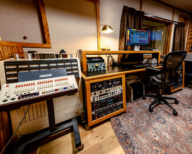 A music recording studio featuring recording equipment, a computer monitor, and mixing consoles arranged around a rug.