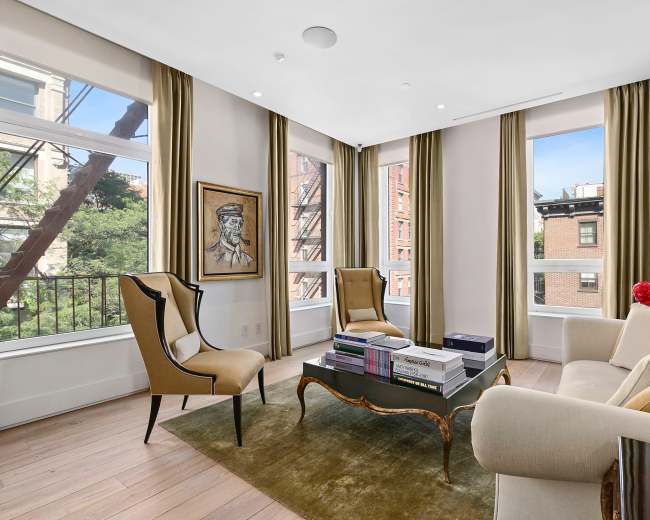 A bright living room with large windows, two armchairs, a sofa, and a coffee table displaying books.