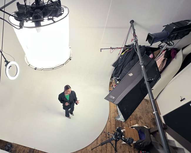 A person stands in a studio with a circular white backdrop, surrounded by studio lighting and camera equipment.