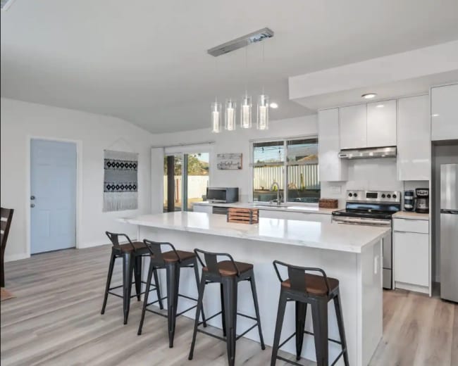 A modern kitchen features a large island with bar stools, stainless steel appliances, and ample natural light from the windows.