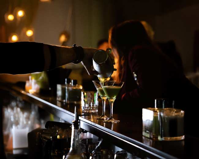 A bartender pours a cocktail into a glass at a dimly lit bar.