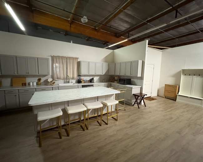 The image depicts a spacious kitchen with gray cabinets, a large white island with four stools, and natural light streaming through a window.