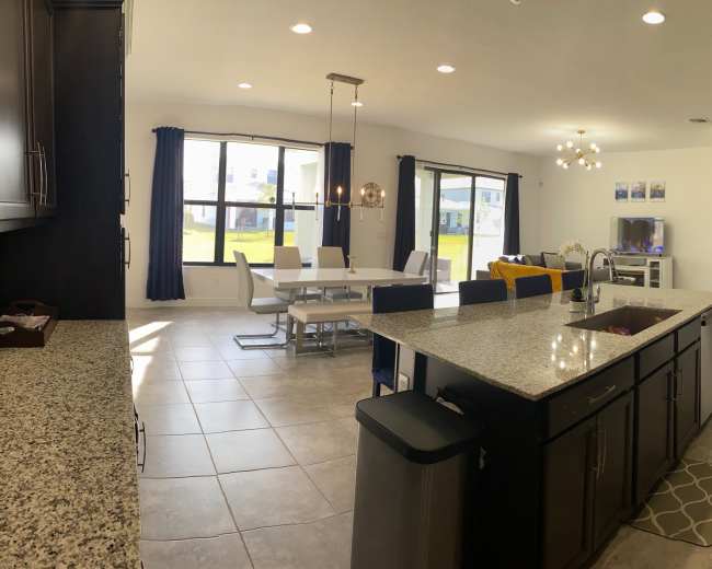A modern kitchen with granite countertops opens to a dining area and living room, featuring large windows that provide natural light.