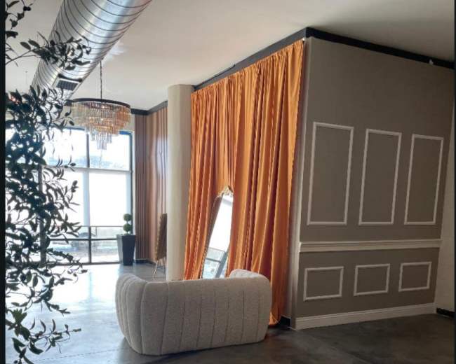 The image shows an interior space featuring a curved white couch, orange curtains, large windows, and a decorative mirror against a wall with paneling.