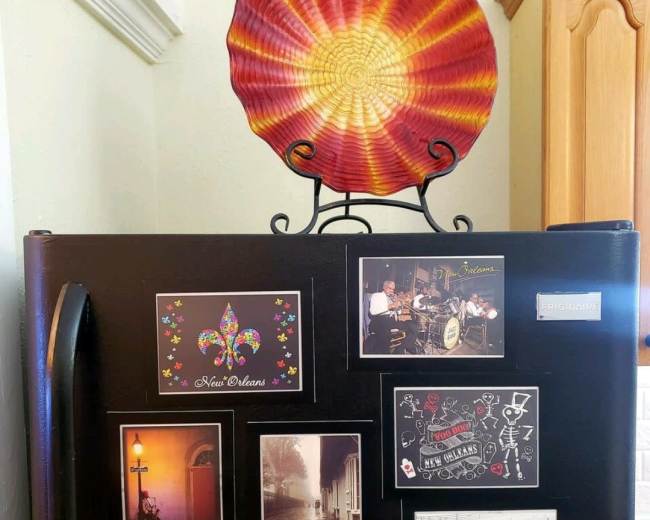 A black refrigerator is decorated with postcards and a colorful decorative plate on a wire rack above it.