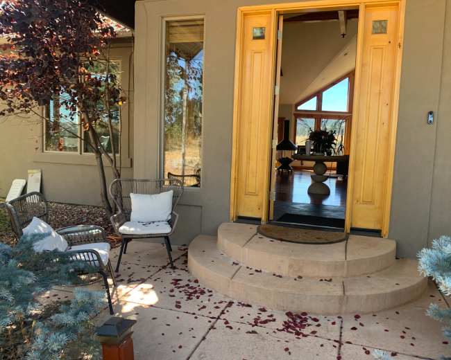 The image shows a front entrance with yellow double doors, leading into a house, surrounded by a stone pathway and adorned with scattered rose petals.