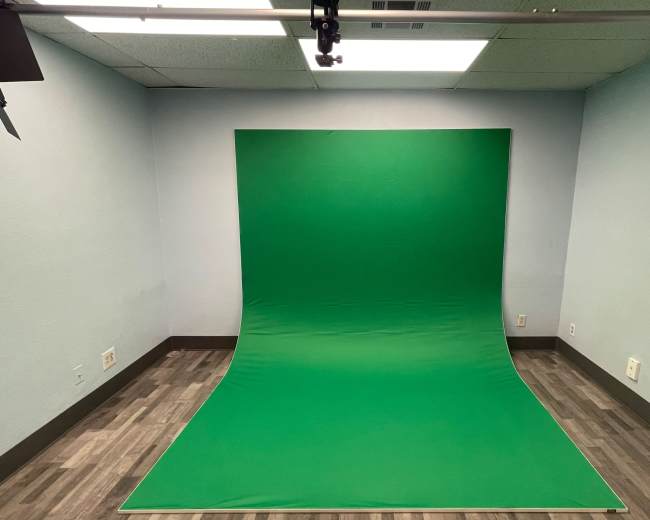 A room with a green screen setup against a light blue wall and a wooden floor.