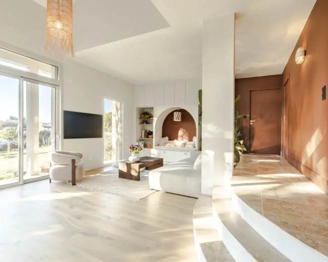 The image shows a modern living room with a large window, a circular arch seating area, a minimalist coffee table, and a combination of light and earthy-colored walls.