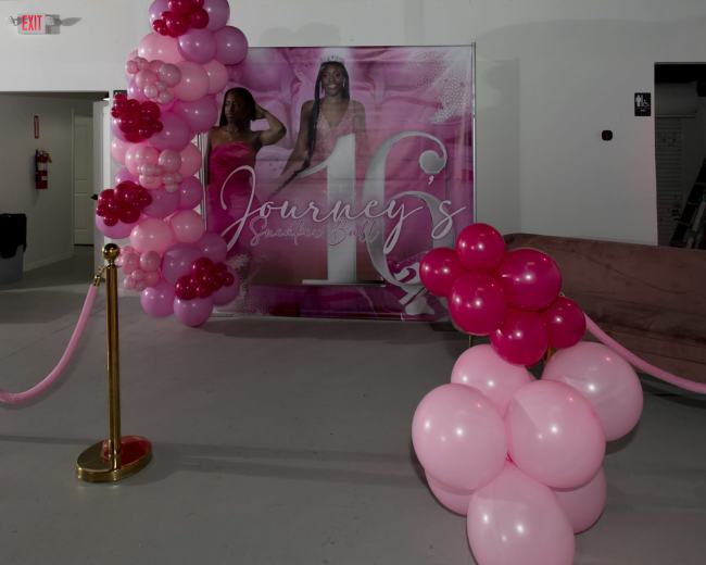 A decorated area featuring a pink balloon arch and a backdrop with the words "Journey's" for a celebration event.