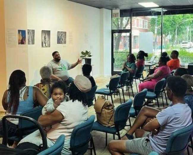 A speaker addresses an audience seated in a community space filled with natural light.