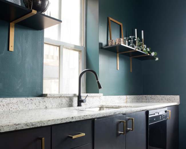 The kitchen features dark cabinetry, a speckled countertop, and wall-mounted shelves above a sink and dishwasher.