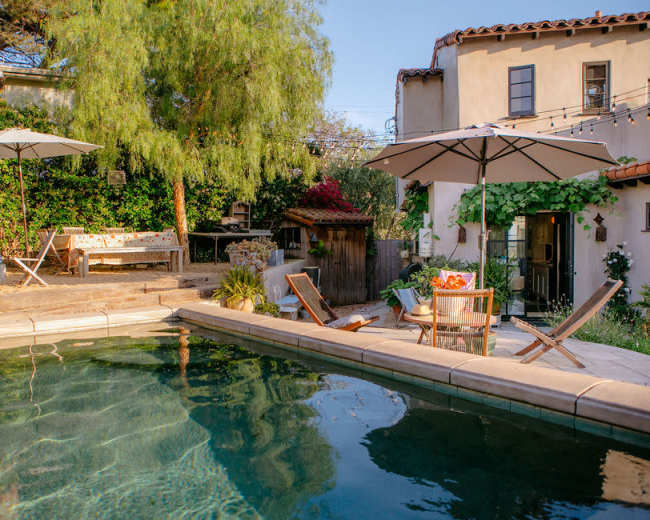The image shows a backyard pool area featuring lounge chairs, umbrellas, and landscaped greenery.