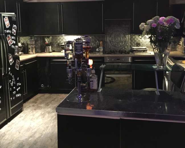 A modern kitchen with black cabinetry, a dark countertop, and a decorative bar setup with bottles and a vase of flowers.