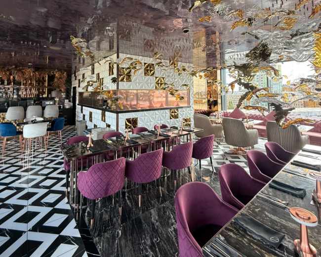 The image shows a stylish restaurant interior featuring a patterned black and white floor, plush purple seating, and a reflective ceiling adorned with decorative elements.