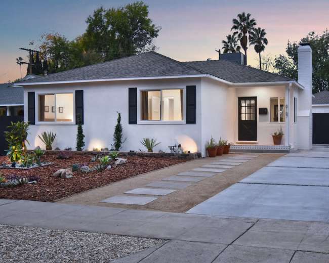The image shows a modern house with a well-maintained front yard, featuring a mix of gravel and concrete pathways leading up to the entrance.