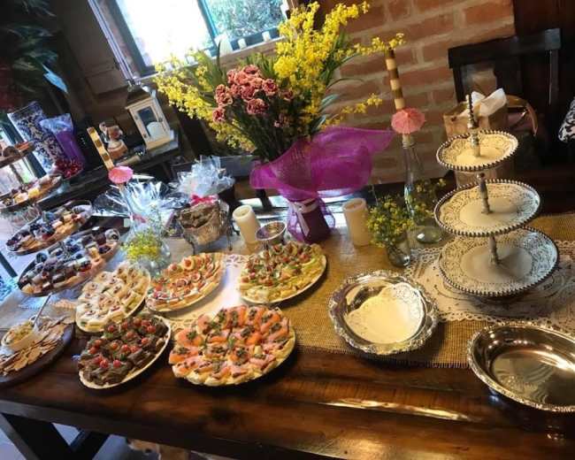 A table is set with an array of decorated dishes featuring various pastries, fruits, and desserts, surrounded by floral arrangements and candles.