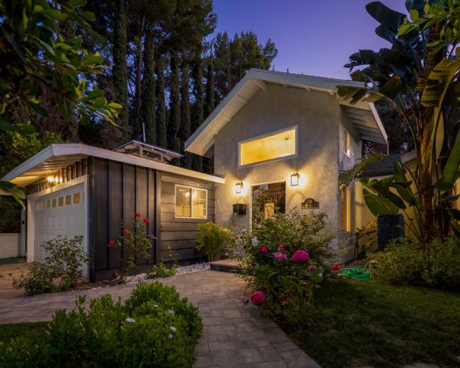 A two-story house with a gray exterior, front garden, and a driveway leads up to a garage.