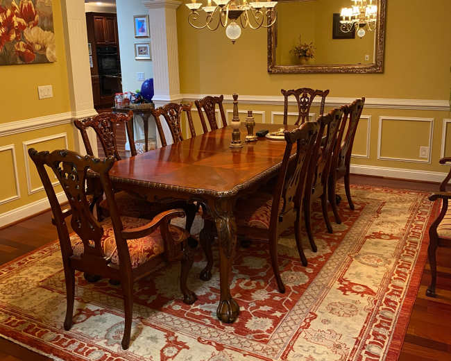 The dining room features a long wooden table surrounded by ornate chairs, with a chandelier overhead and a large framed mirror on the wall.
