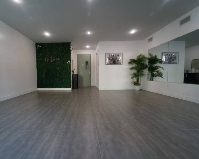 An empty room with grey tile flooring, a welcome-themed green wall, a mirror, and a door at the far end.