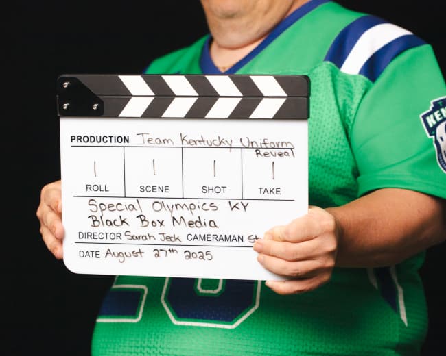 A person holds a movie clapperboard with production details for a "Team Kentucky Uniform Reveal" for Special Olympics Kentucky dated August 27, 2025.