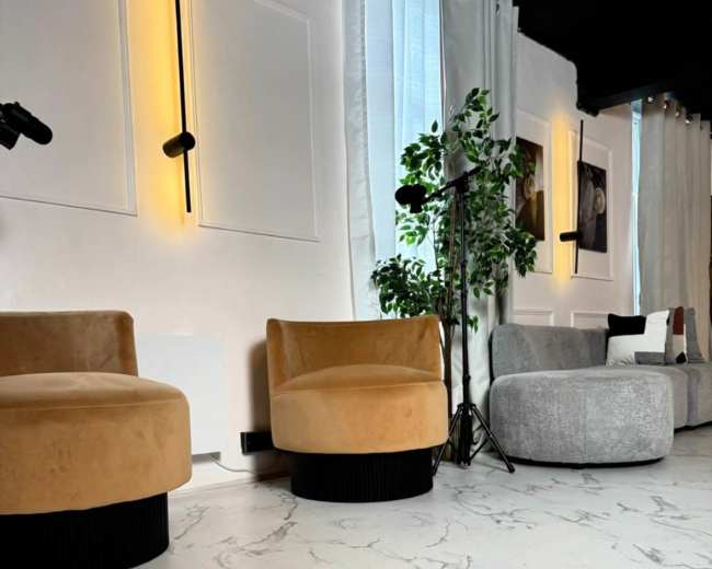 The image features a stylish interior with two plush chairs, a gray sofa, and large windows draped with curtains, set against a marble-patterned floor.