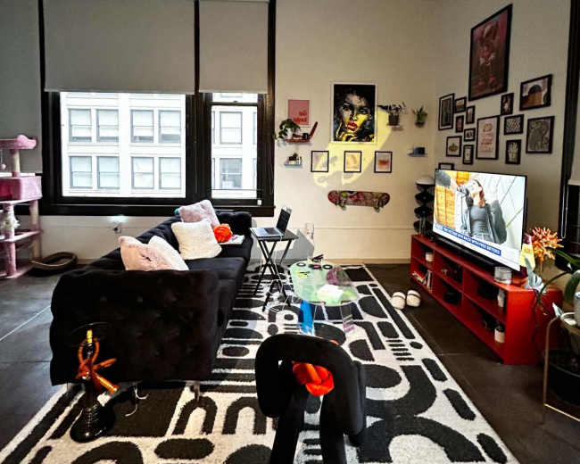 A cozy living room features a black sofa, a red TV stand, and walls adorned with framed pictures, while a television displays a show in the background.