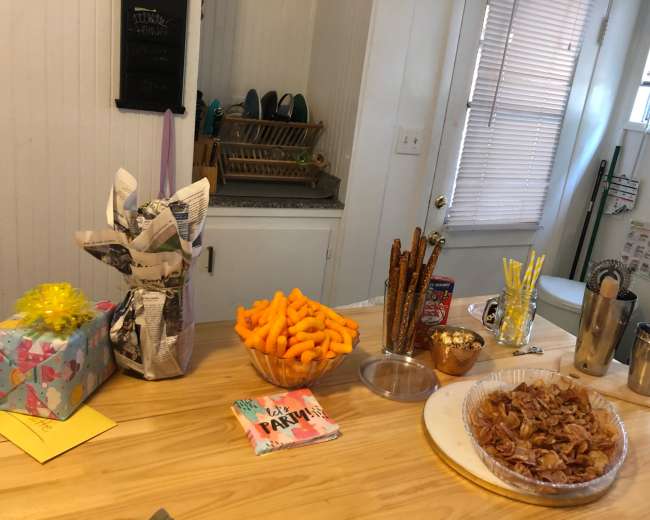 A table is set up with snacks including cheese puffs, pretzels, popcorn, and a tray of bacon, alongside wrapped gifts and a festive card.