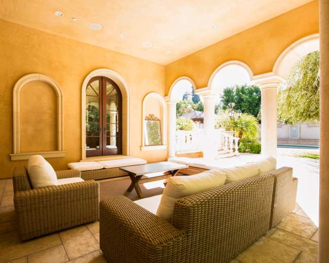 A well-lit outdoor seating area with wicker furniture and arched windows overlooking a garden.