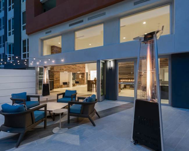 An outdoor seating area with four chairs and a small table, illuminated by string lights, adjacent to a modern building.
