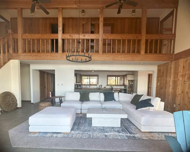 A spacious living room featuring a large sectional sofa, wooden beams, and a kitchen area visible in the background.
