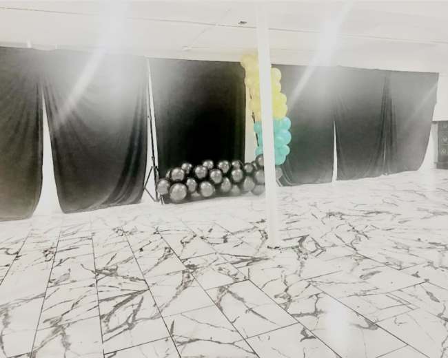 A spacious interior with a marbled floor, black drapes, and a cluster of balloons in teal and yellow on one side.