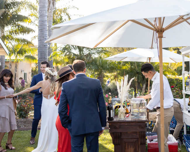 A group of people mingles near a bar setup in a garden during a daytime event.