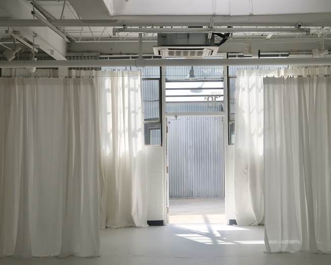 A spacious room with white curtains dividing areas and an open doorway leading to an outdoor space.