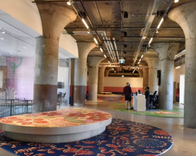The image shows a spacious interior with concrete pillars and colorful patterned flooring in a modern building.