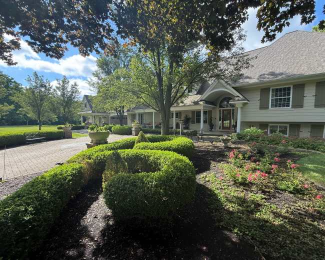 A spacious house with a landscaped front yard featuring hedges, flower beds, and a pathway.