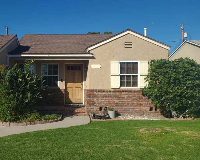 The image shows a single-story house with a brick and stucco exterior, a front yard with grass, and a driveway leading to a garage.